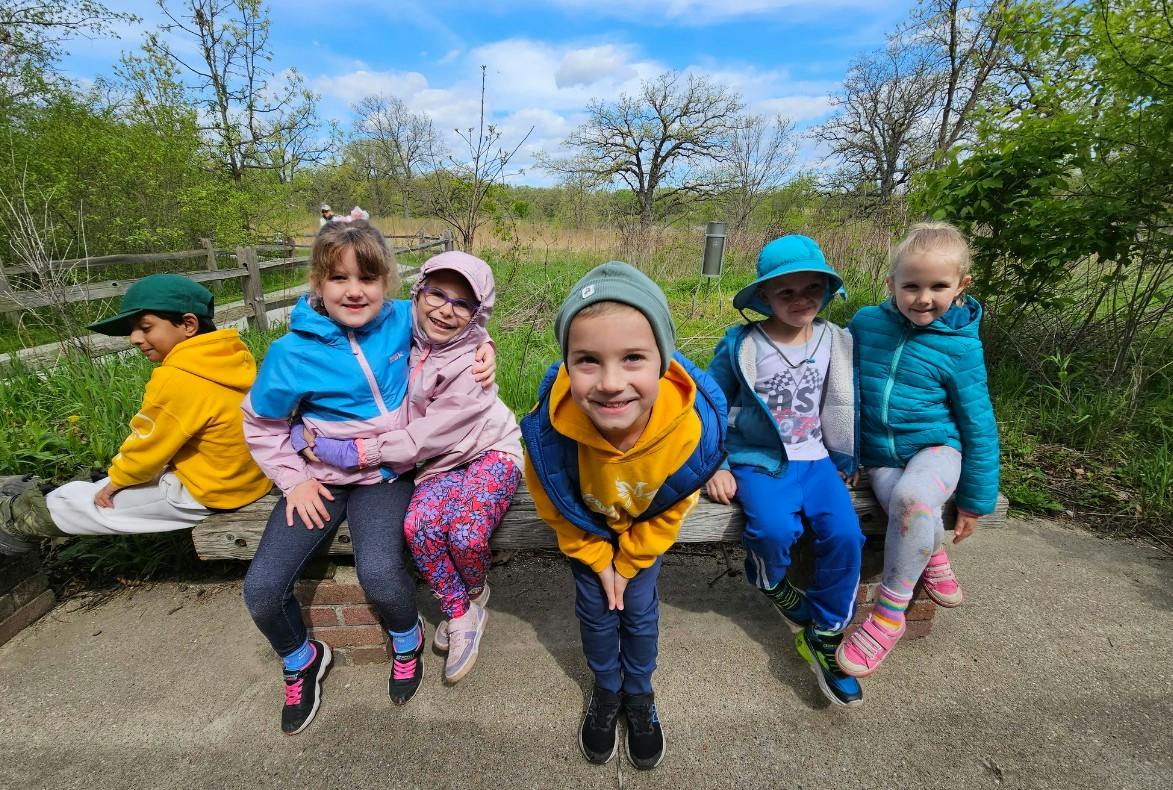 Group of children sitting on a wooden bench outdoors