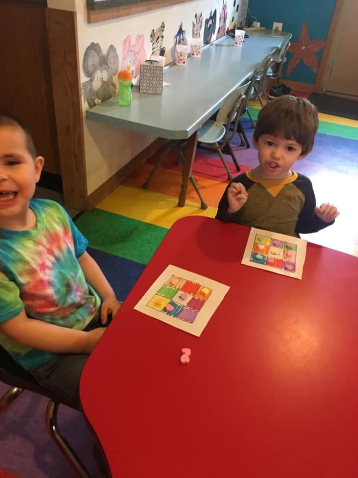 Two children sitting at a red table with colorful artwork