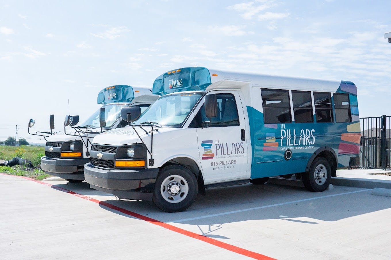 Two white and teal shuttle buses branded with The Pillars Christian Learning Centers