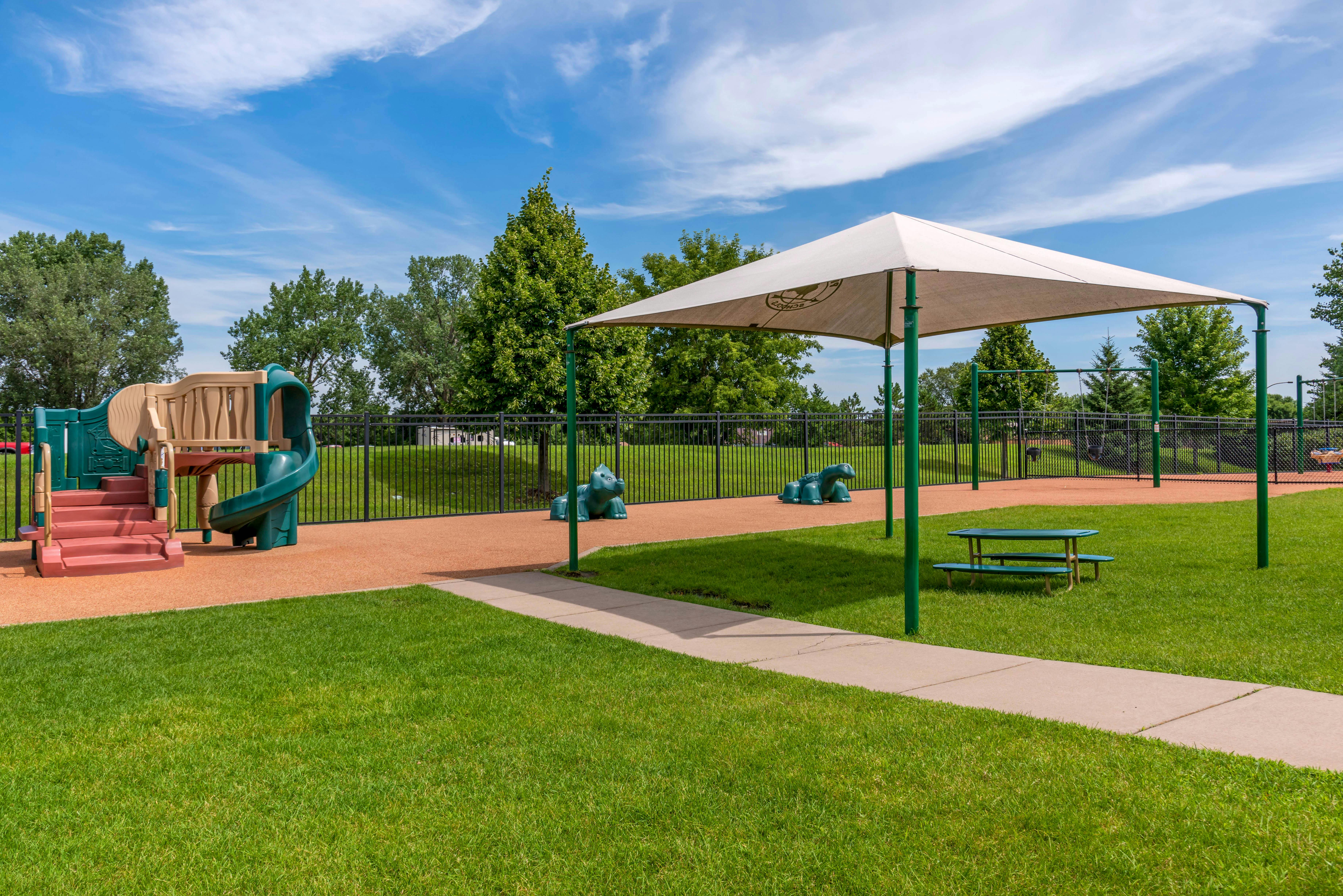 Playground with climbing structure, slide, swings, and shade structure