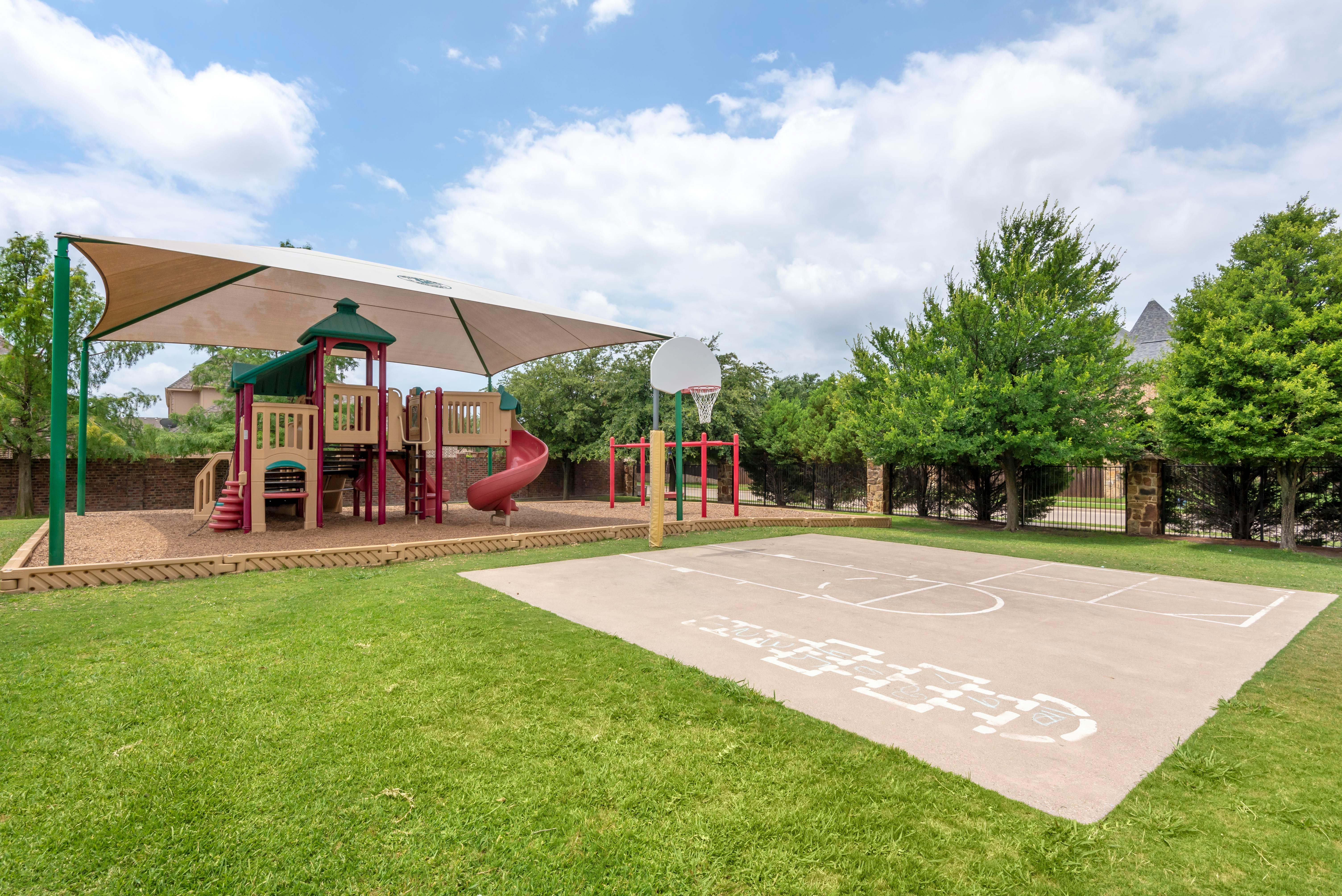 Playground with playset under a shade canopy, basketball hoop, and painted court
