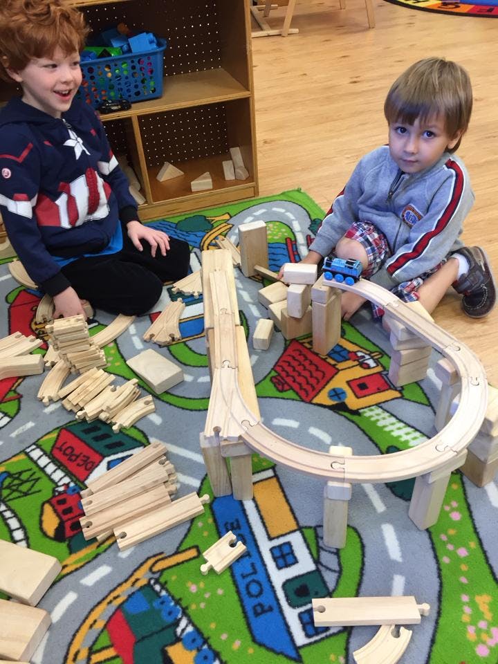 Two children playing with a wooden train set on a rug