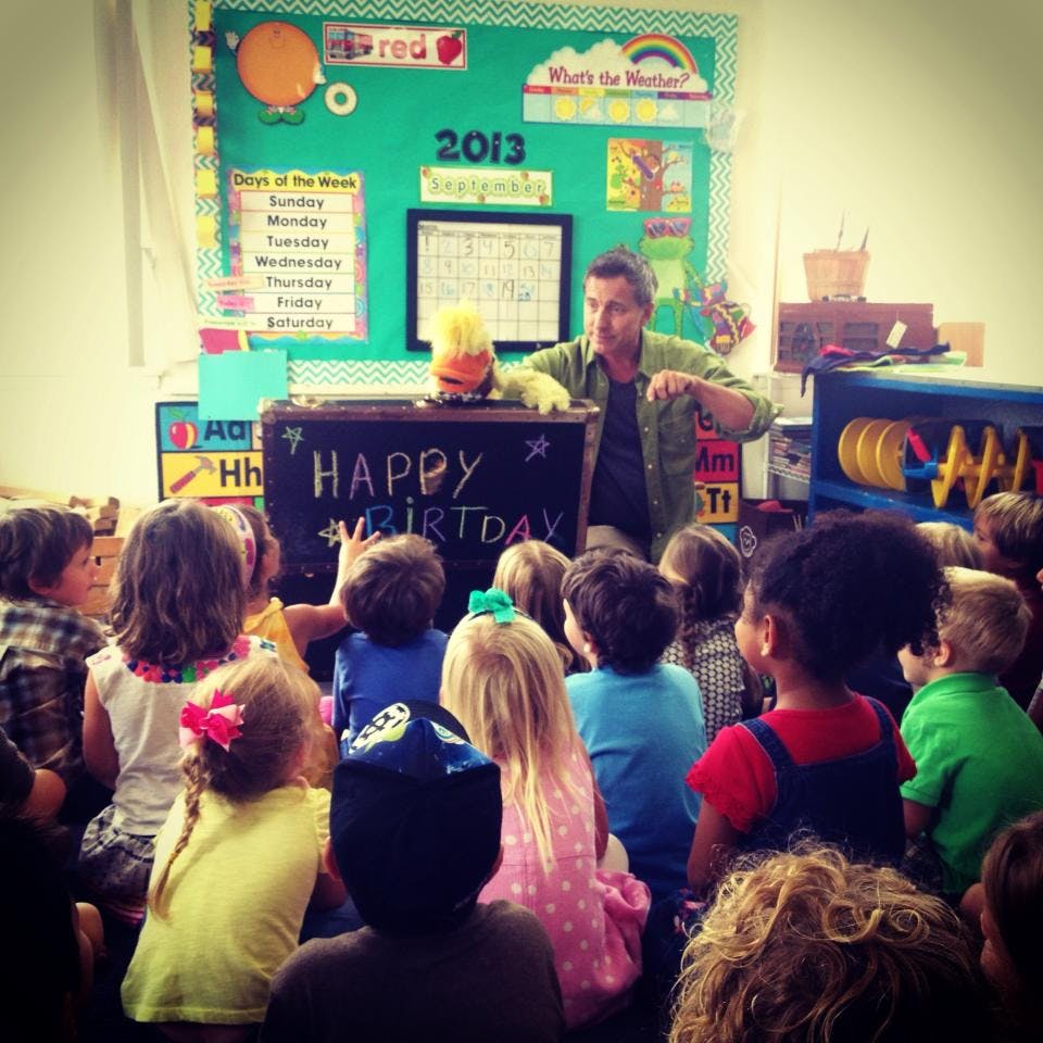 Person with a puppet performing for a group of children in a classroom