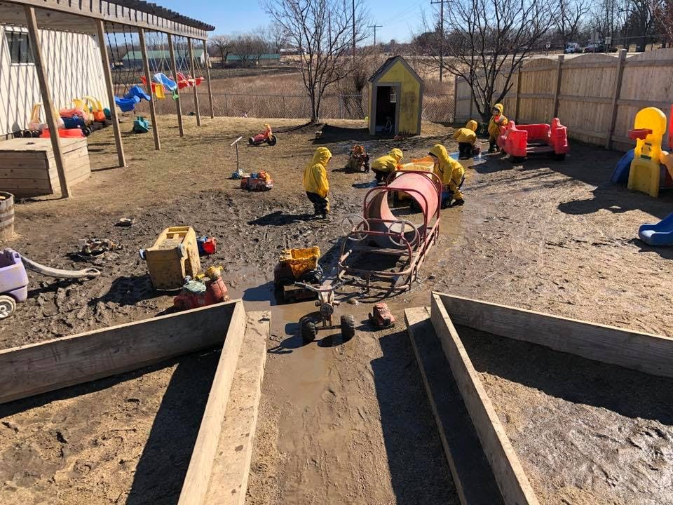 Children playing in a muddy outdoor area with toys