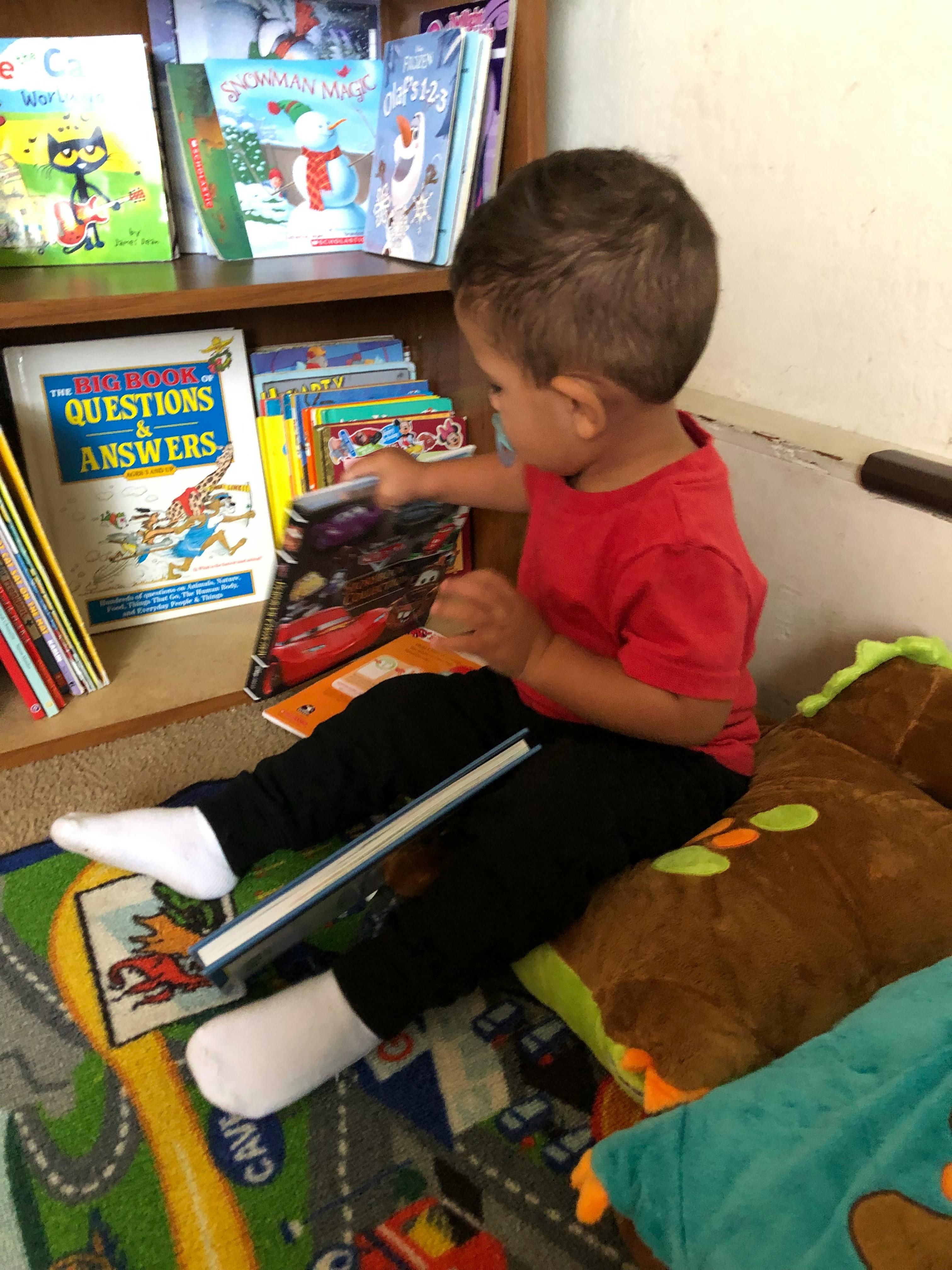 Child sitting on floor reaching for a book on a shelf