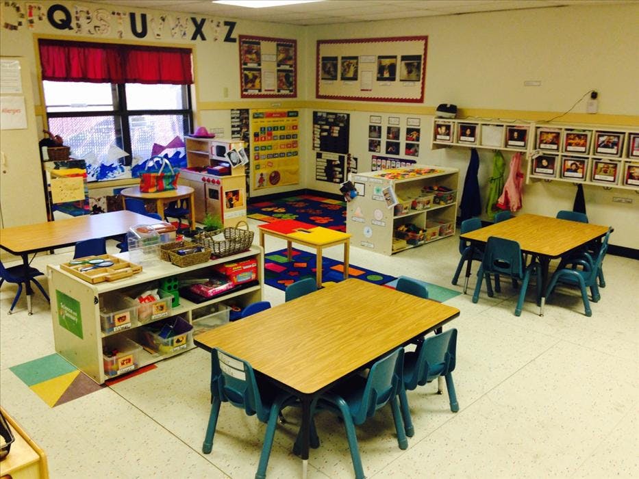 Empty classroom with small tables and chairs, shelves, and learning decorations