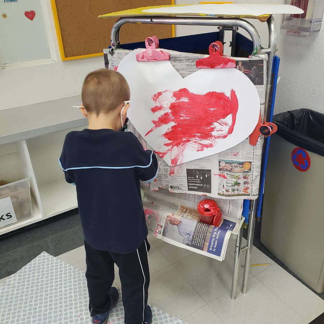Child painting a heart shape on an easel
