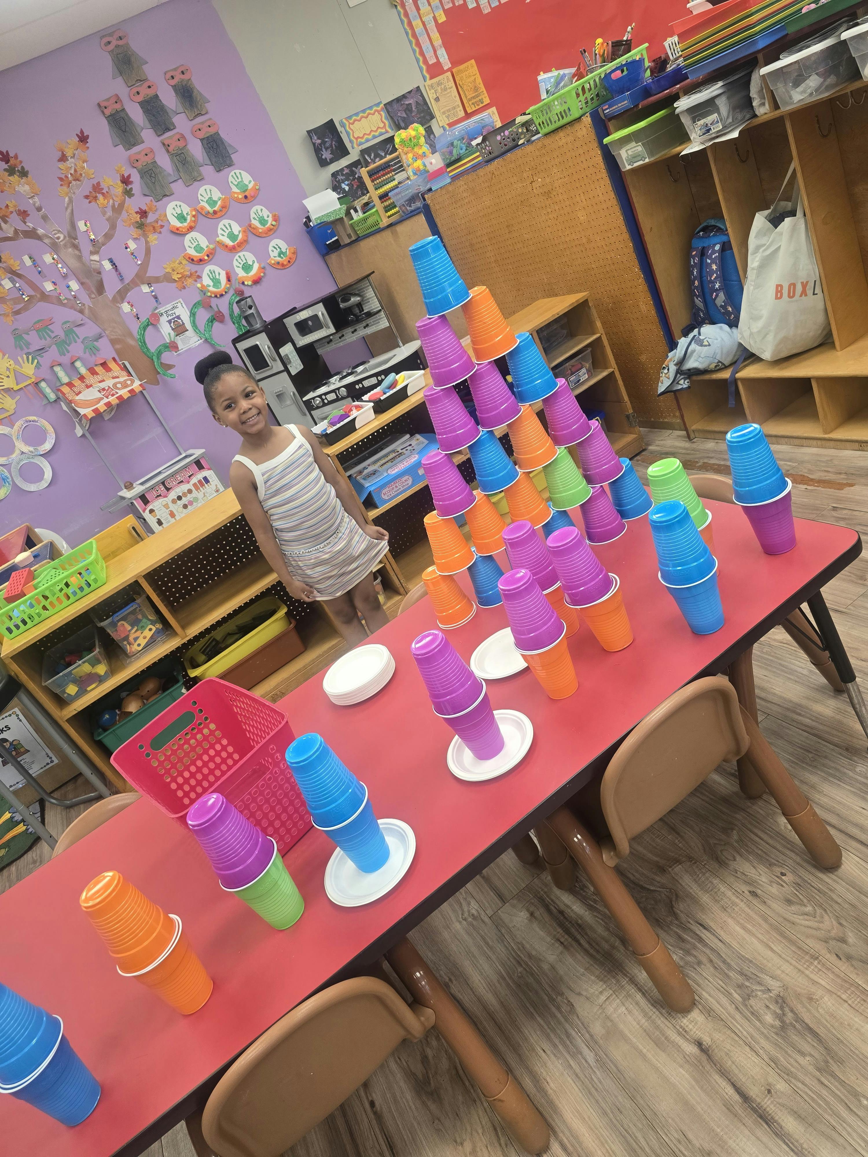 Child standing by a table with a tall stack of colorful plastic cups