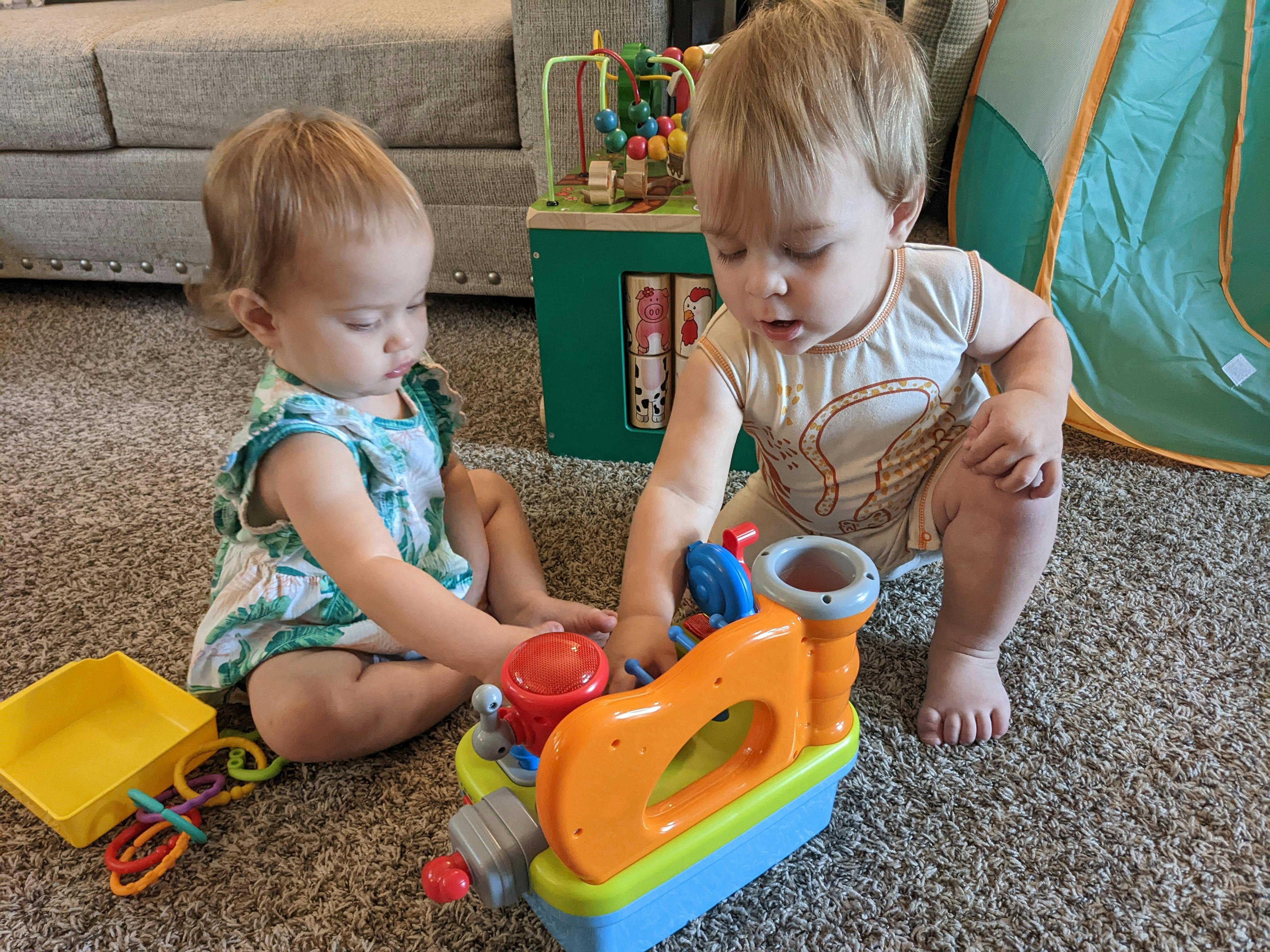 Two children playing with a toy on a carpeted floor