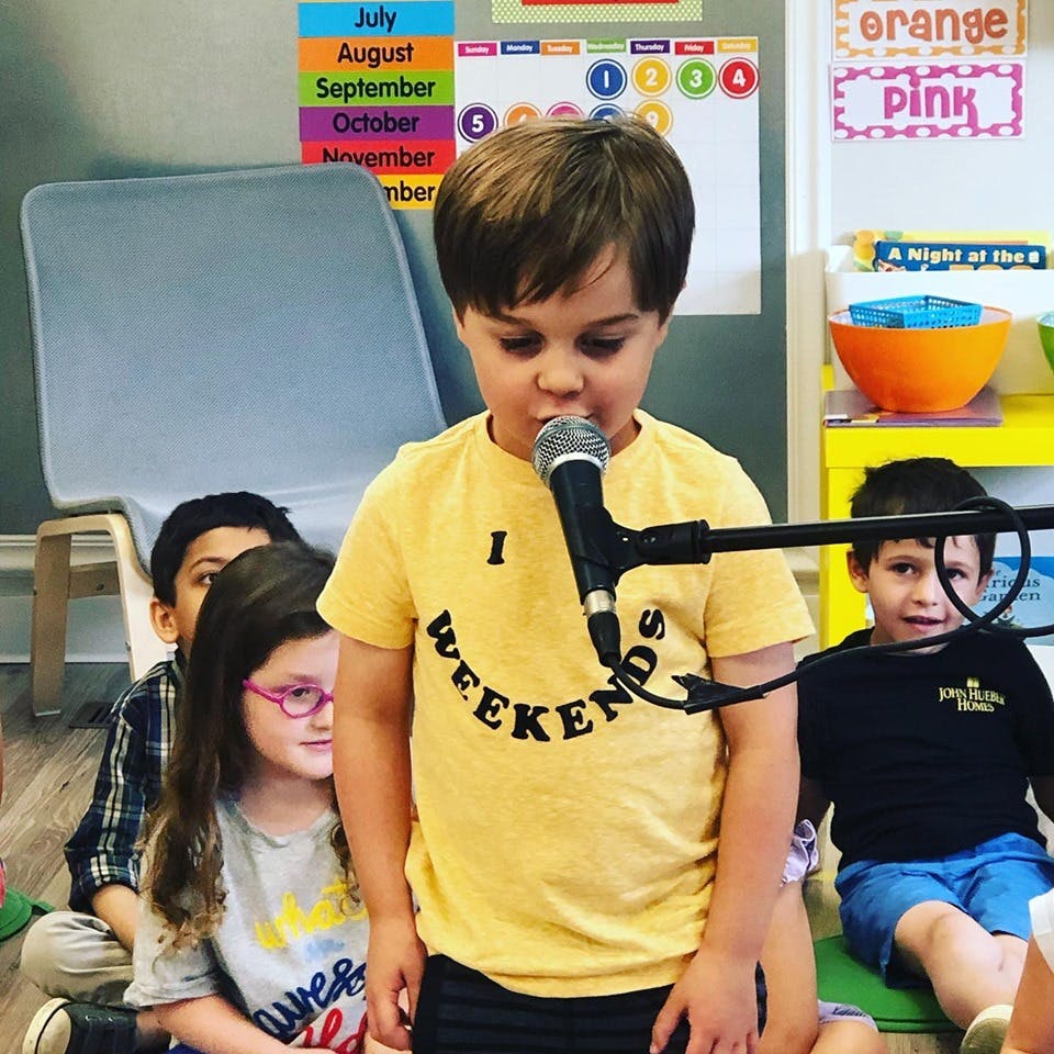 Child speaking into a microphone in a classroom with other children