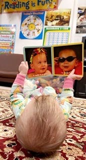 Child lying on back holding up a book with two baby faces