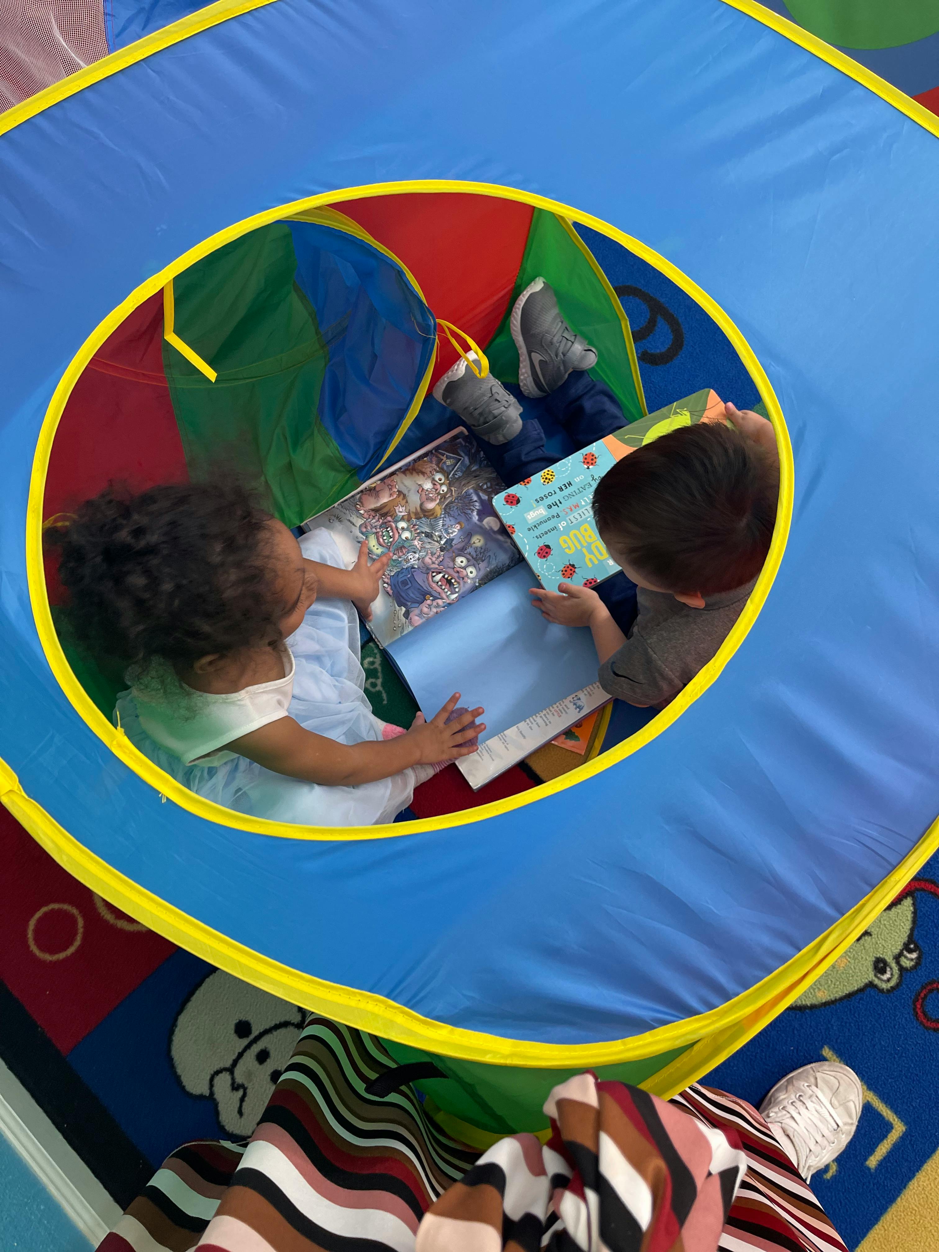 Two children reading books inside a play tent
