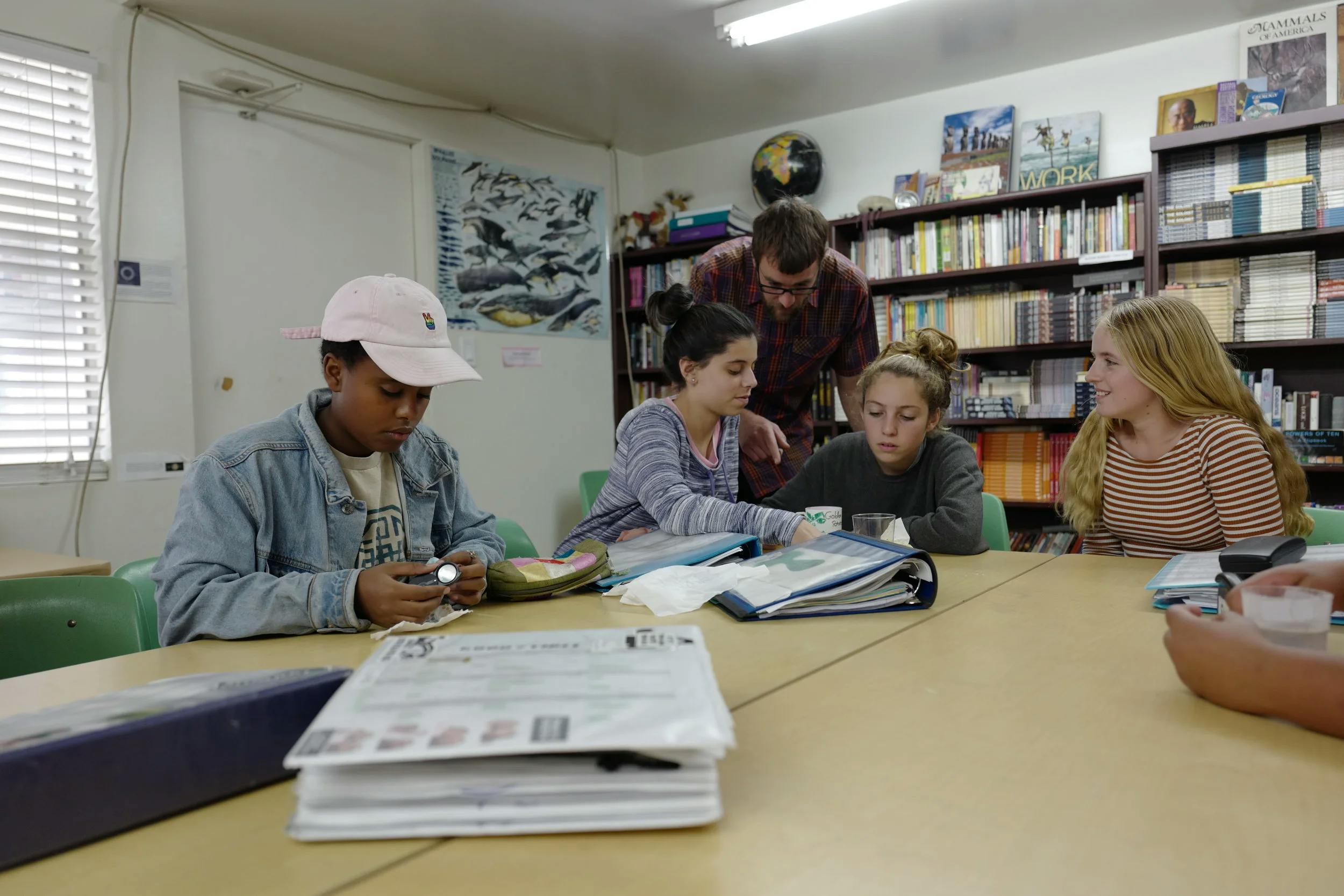 Teacher and three teens looking at an open binder on a table