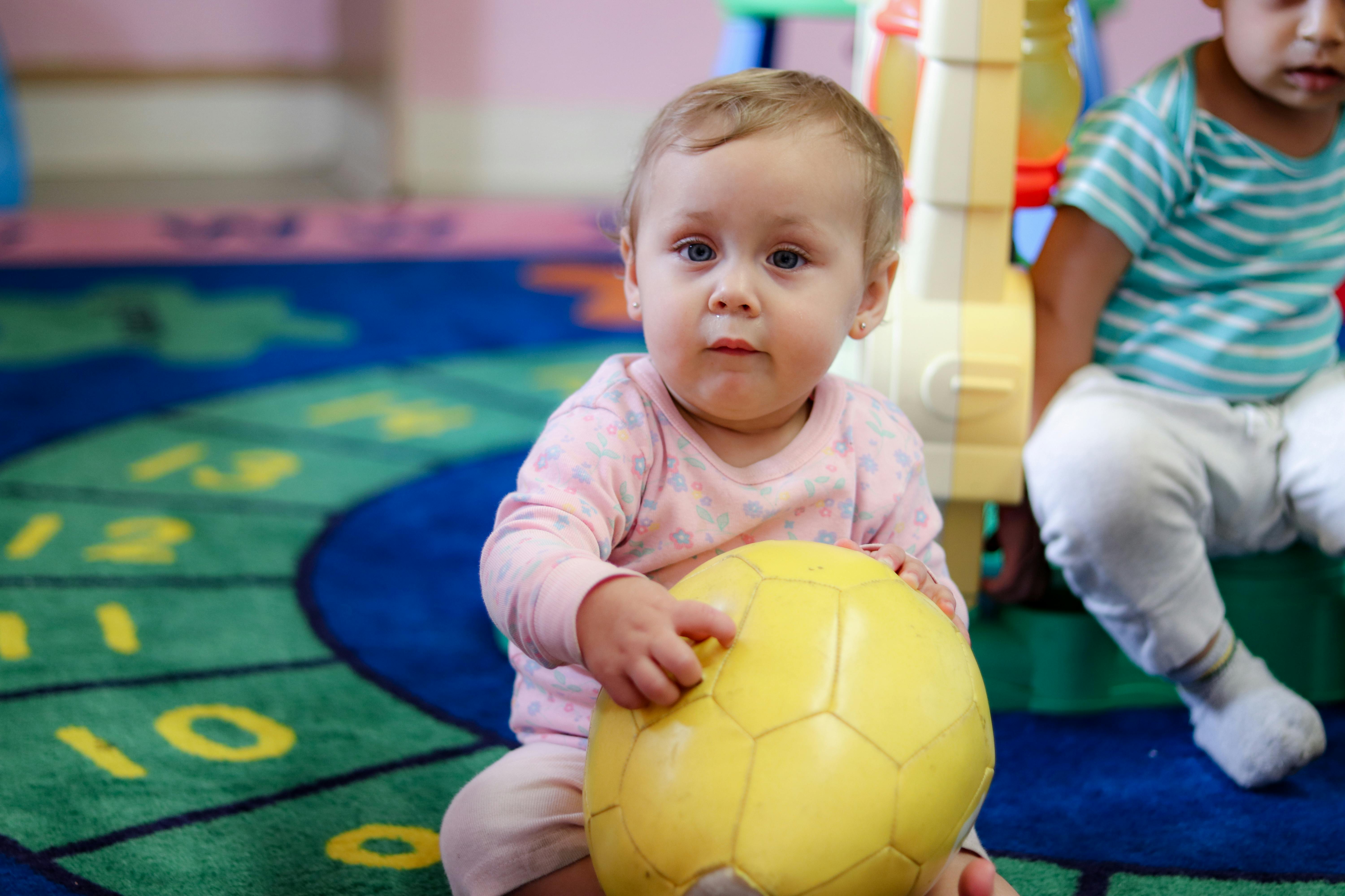 Child holding a yellow ball on a colorful rug