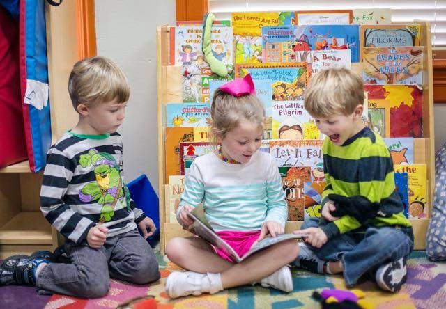 Three children sitting on the floor reading a book in a classroom