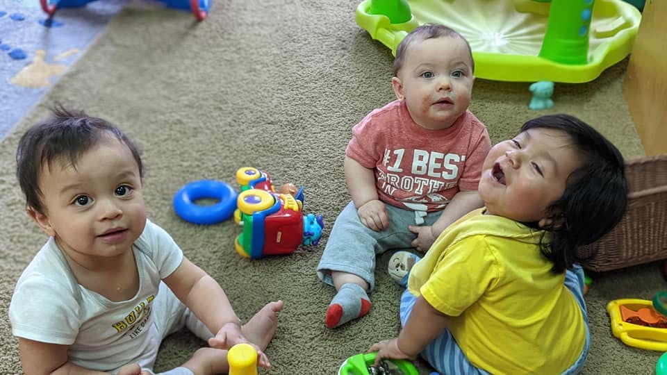 Three babies sitting on a rug with toys