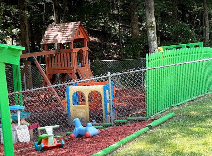 Outdoor playground with wooden playhouse, plastic play structure, and green fence