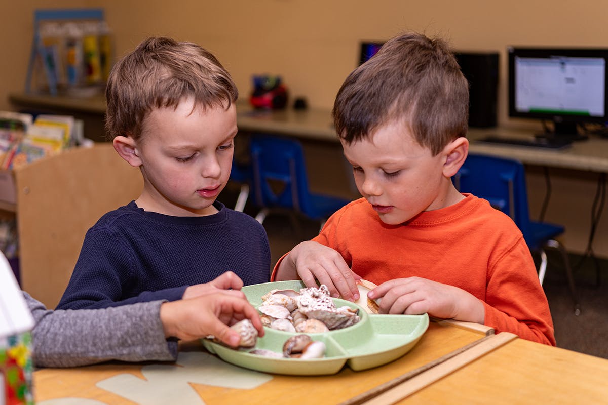 Two children eating snacks from a divided plate