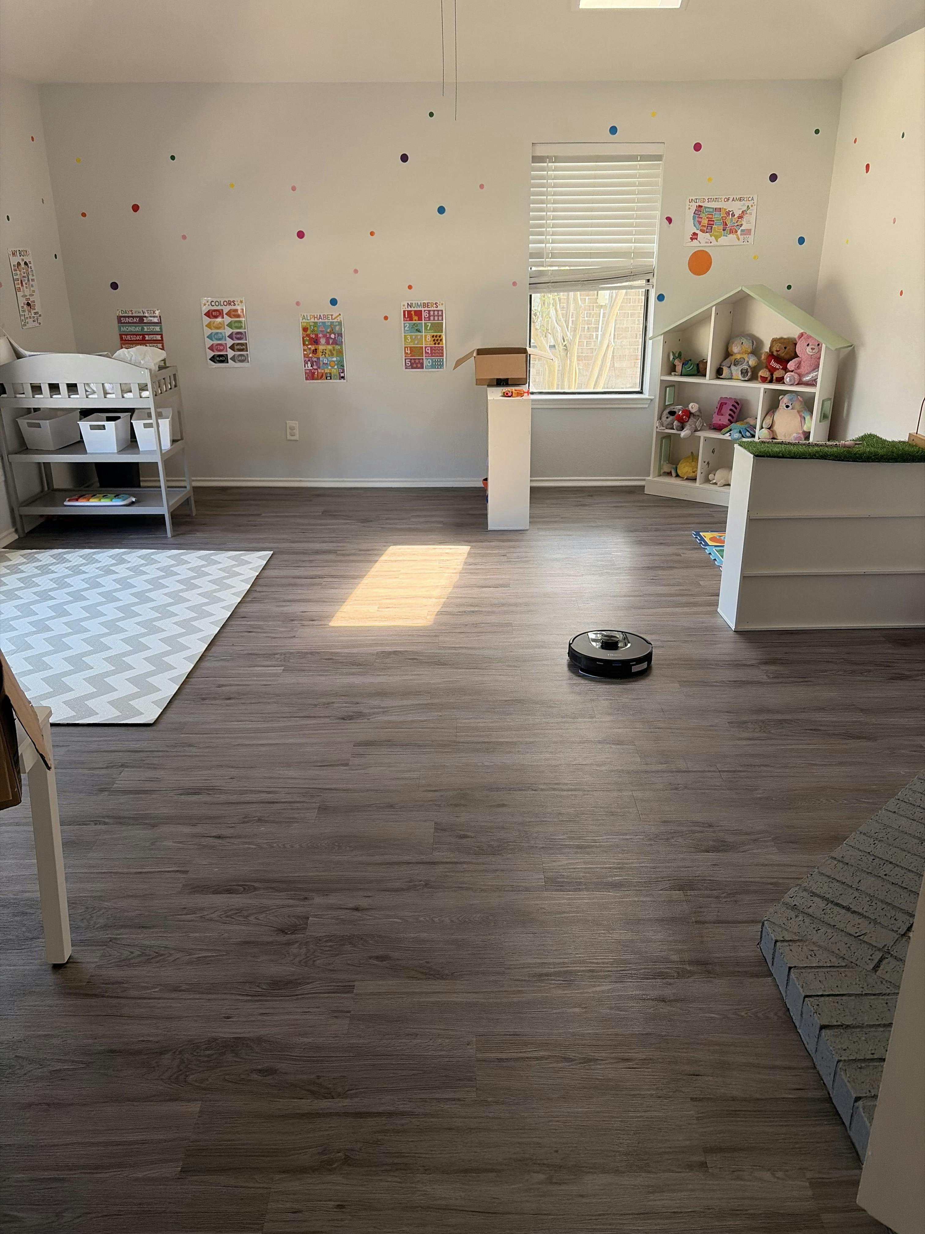 Robot vacuum on floor in a child playroom with shelves and wall decor