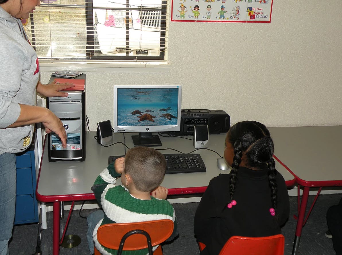 Person helping two children at a computer