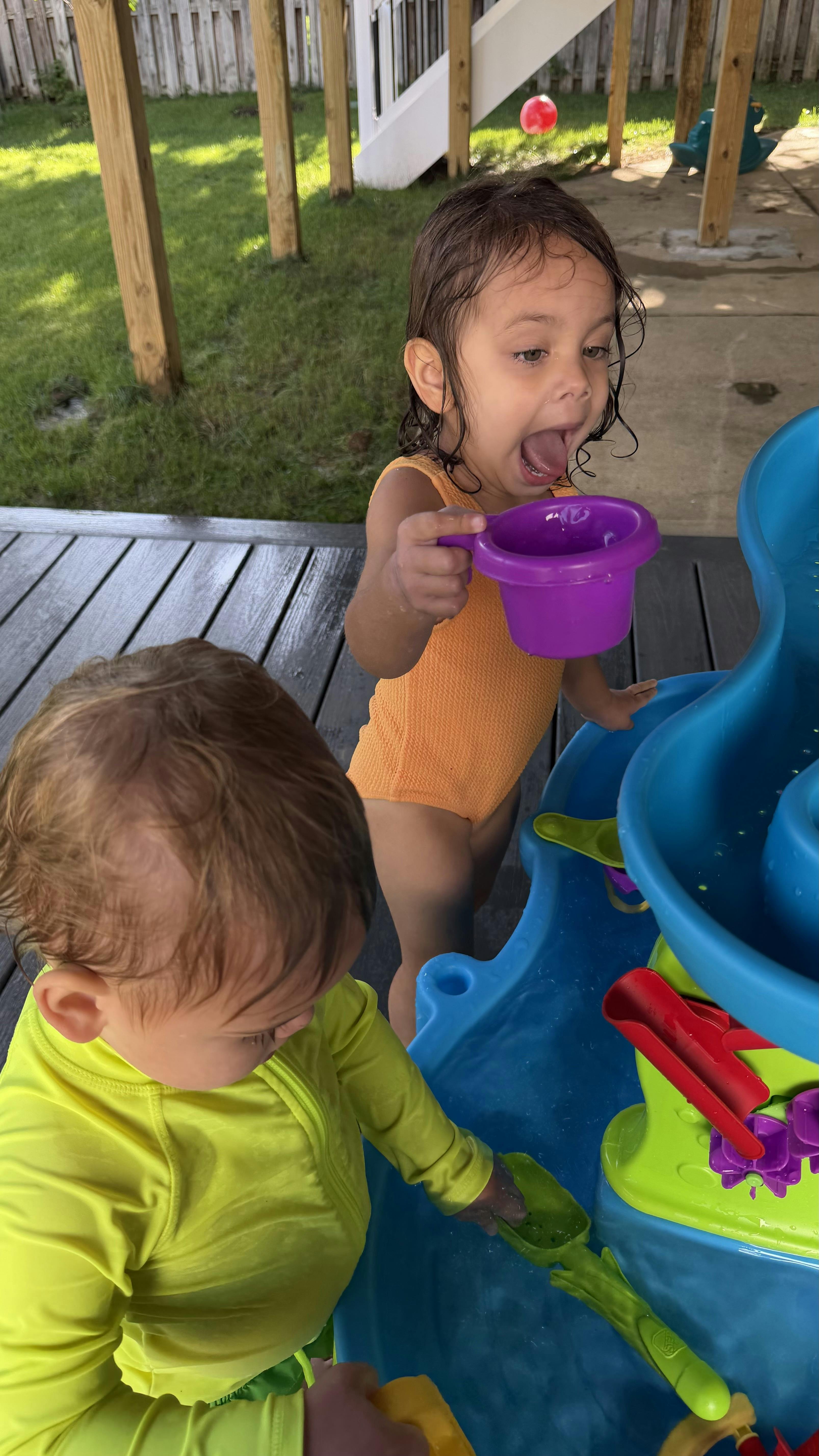 Two children playing at a water table on a wooden deck