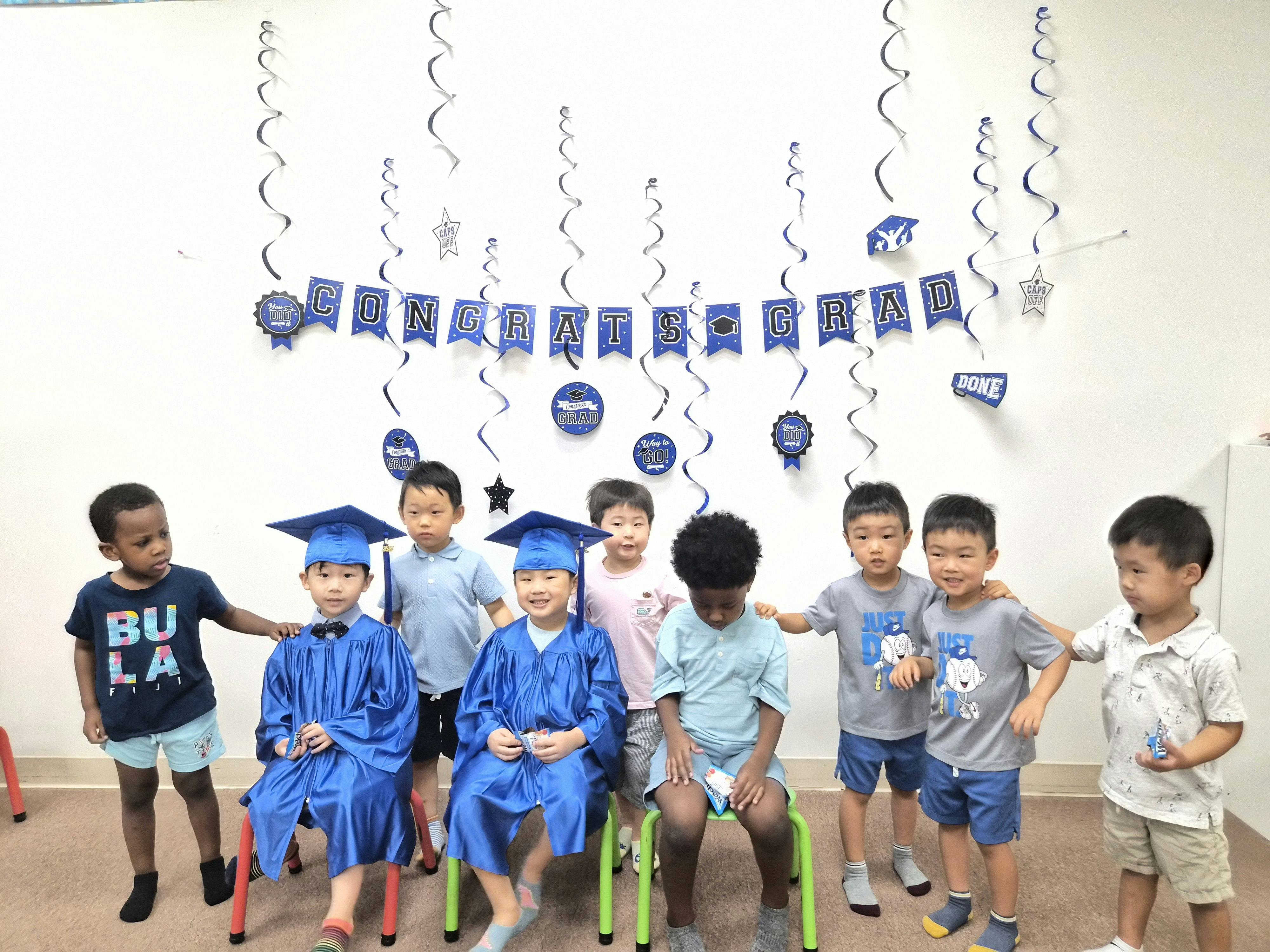 Group of children at a preschool graduation party with Congrats Grad banner