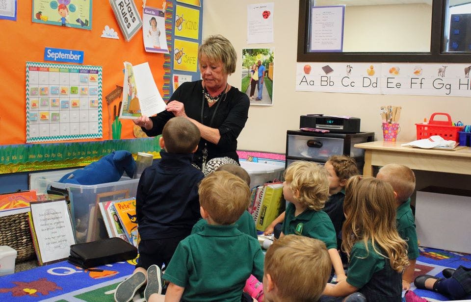 Adult reading a book to a group of children in a classroom