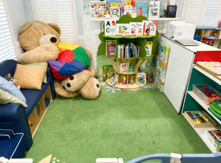 A children's reading area with a large teddy bear and a tree-shaped bookshelf