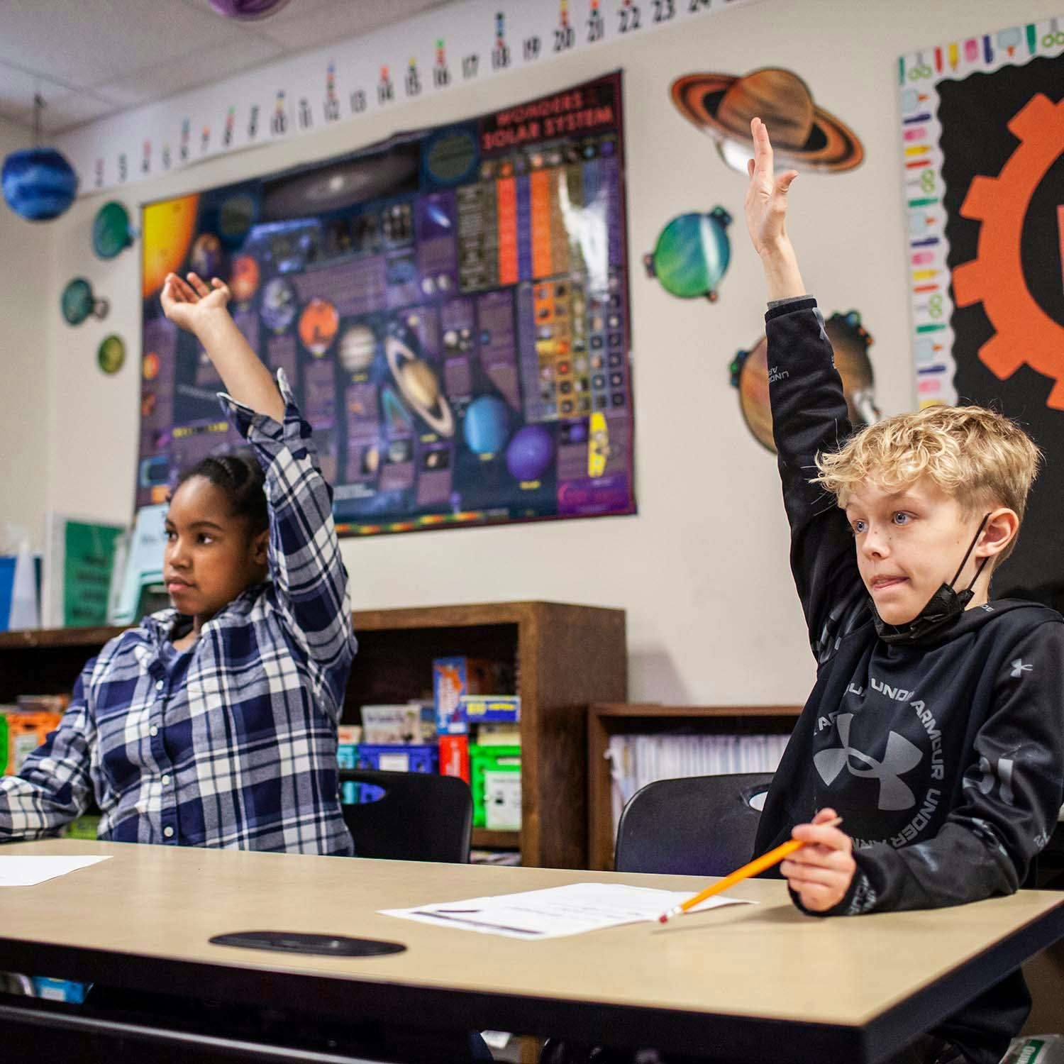Two children raising their hands in a classroom
