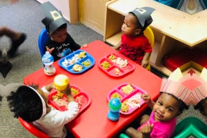 Four children wearing paper hats eating at a red table