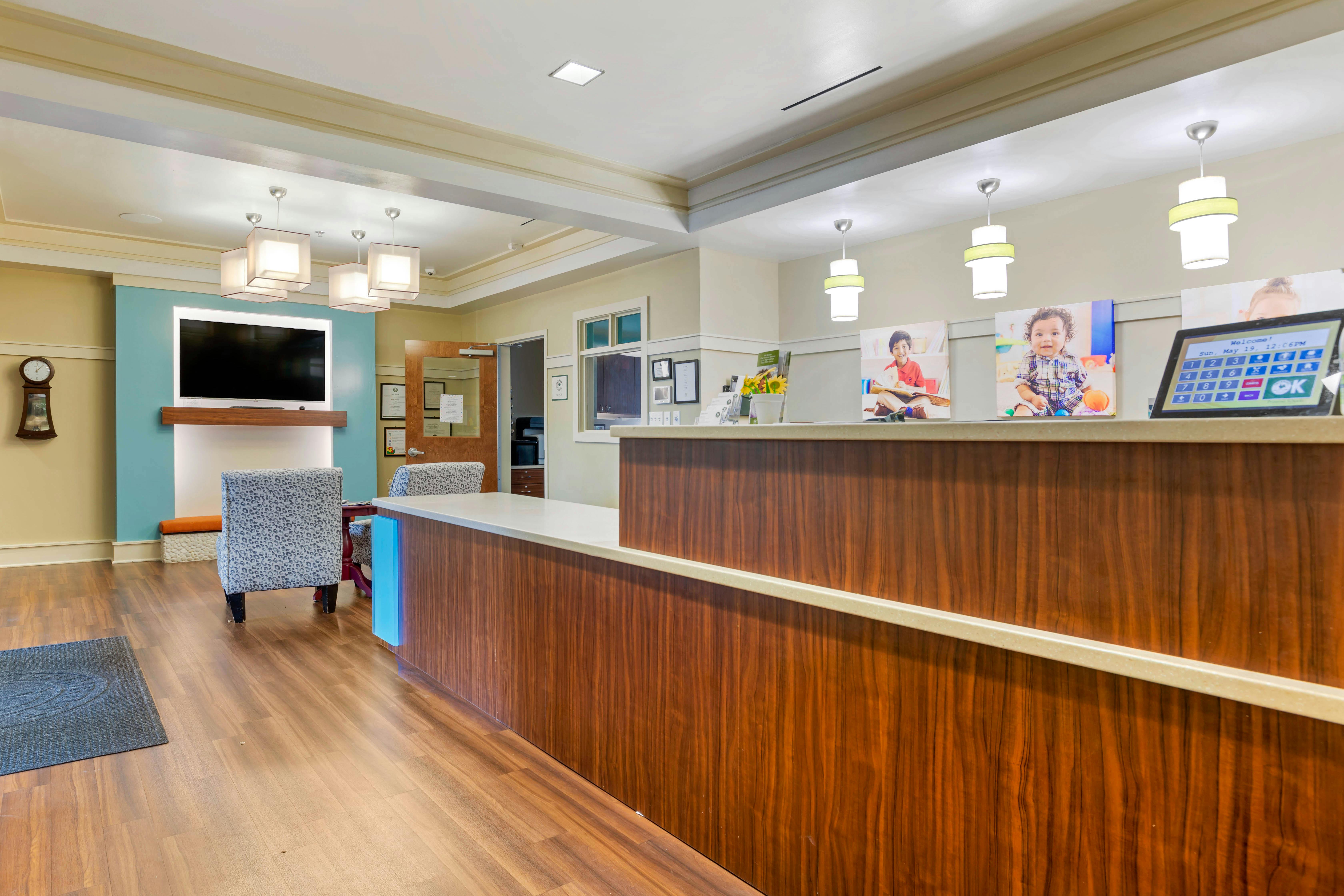 Lobby with a wood reception desk, television, two chairs, and pictures of children