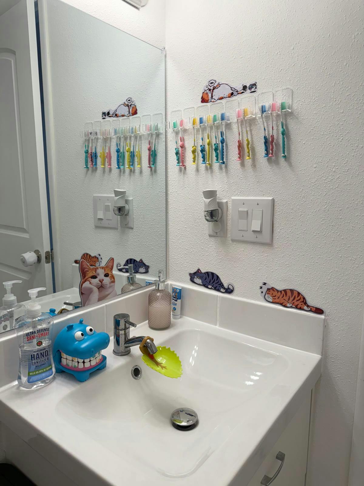 Bathroom sink with toothbrushes hanging on the wall and cat decorations