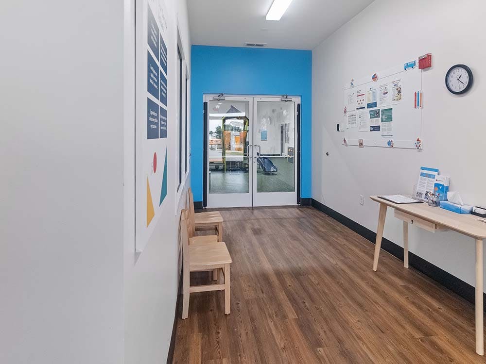 Hallway with wood floors and blue wall accent, two chairs, and an information board