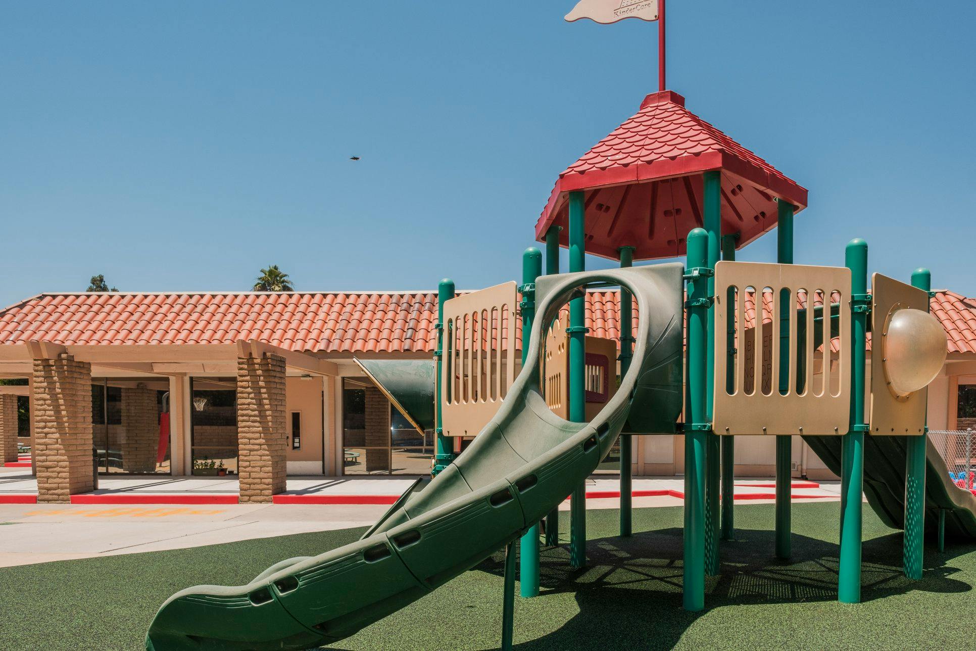 Playground equipment with a green slide and red roof near a building