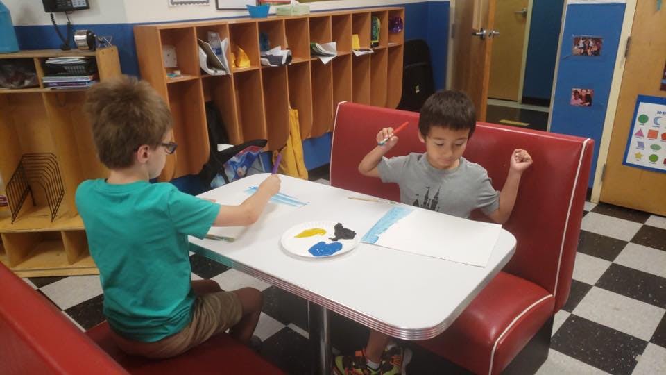 Two children sitting at a table with art supplies