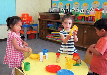 Three children playing with toys around a yellow table