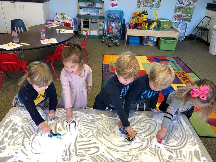 Children playing with shaving cream and toy cars on a table