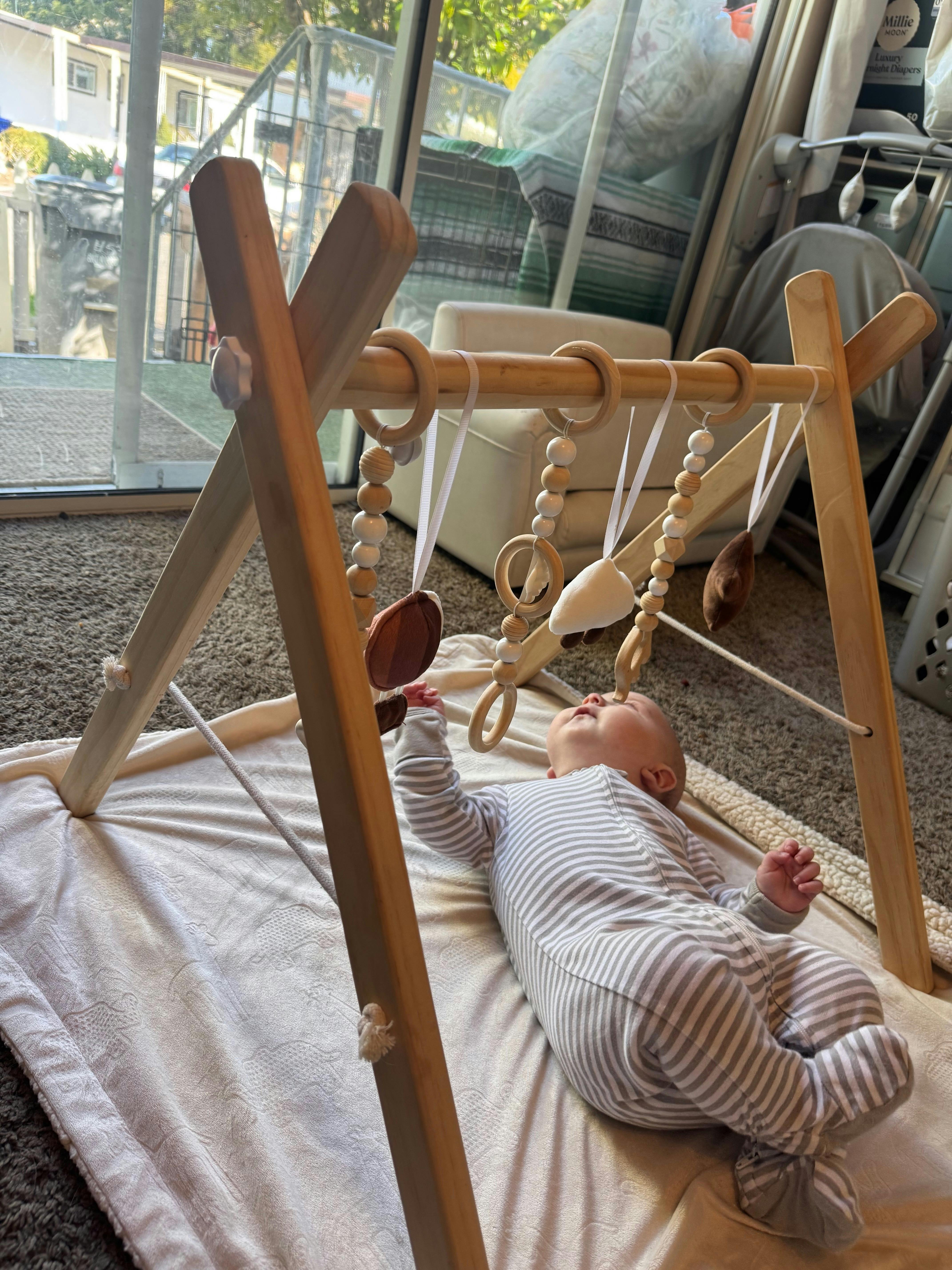 Child lying on a blanket reaching for hanging toys from a wooden play gym