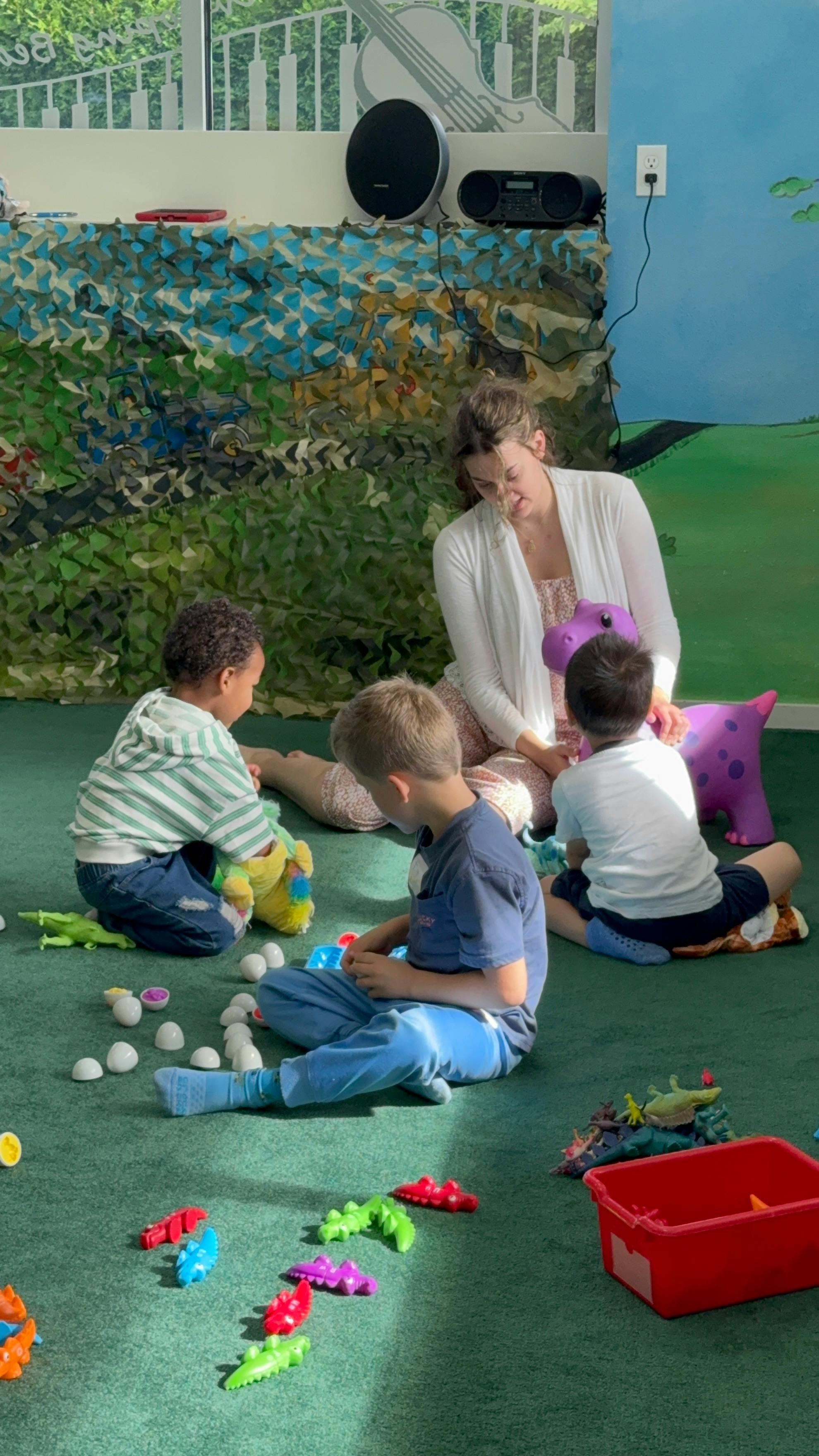Adult and three children sitting on the floor playing with plastic toys