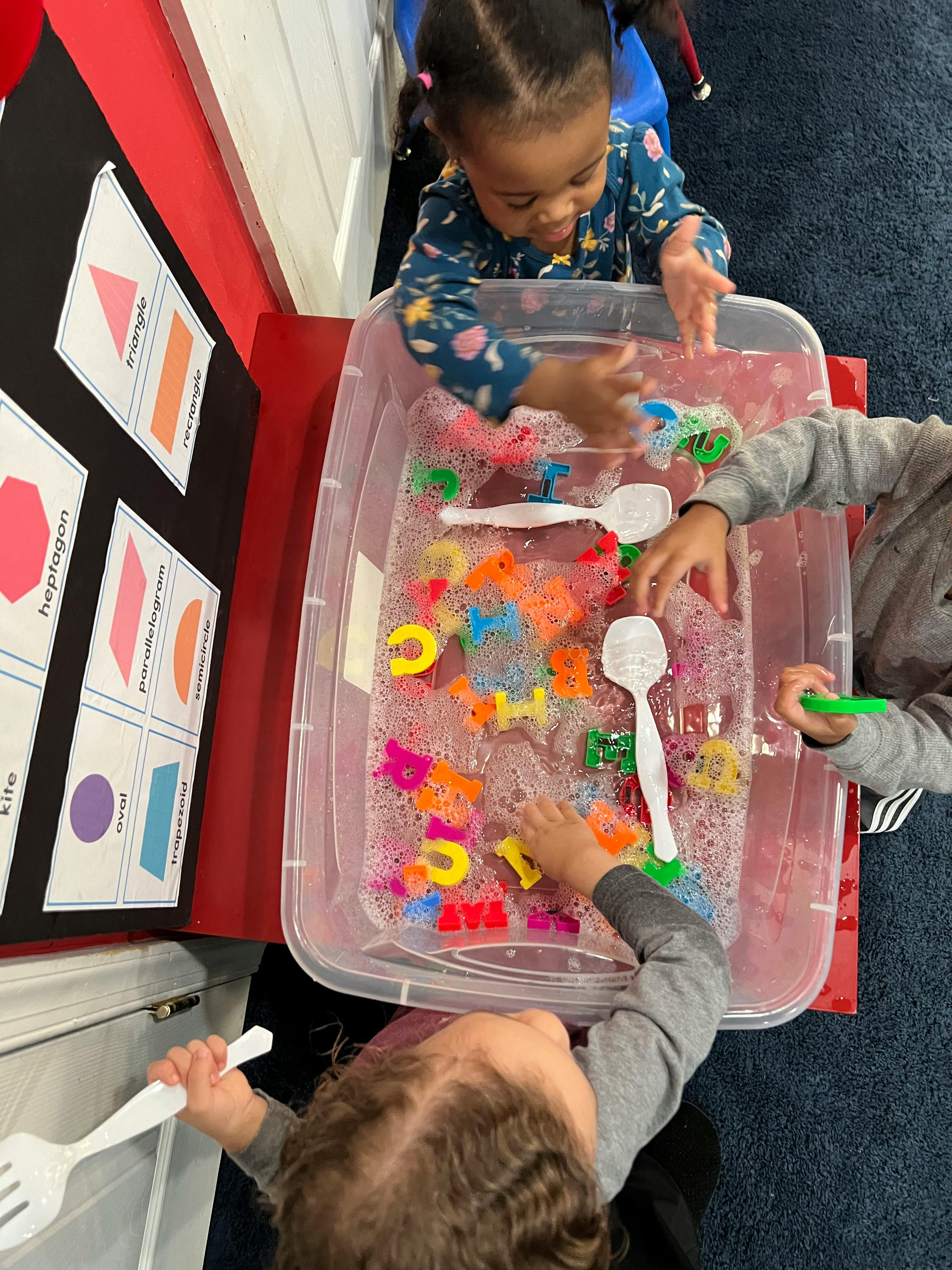 Children playing with colorful letters and toys in a sensory bin with water