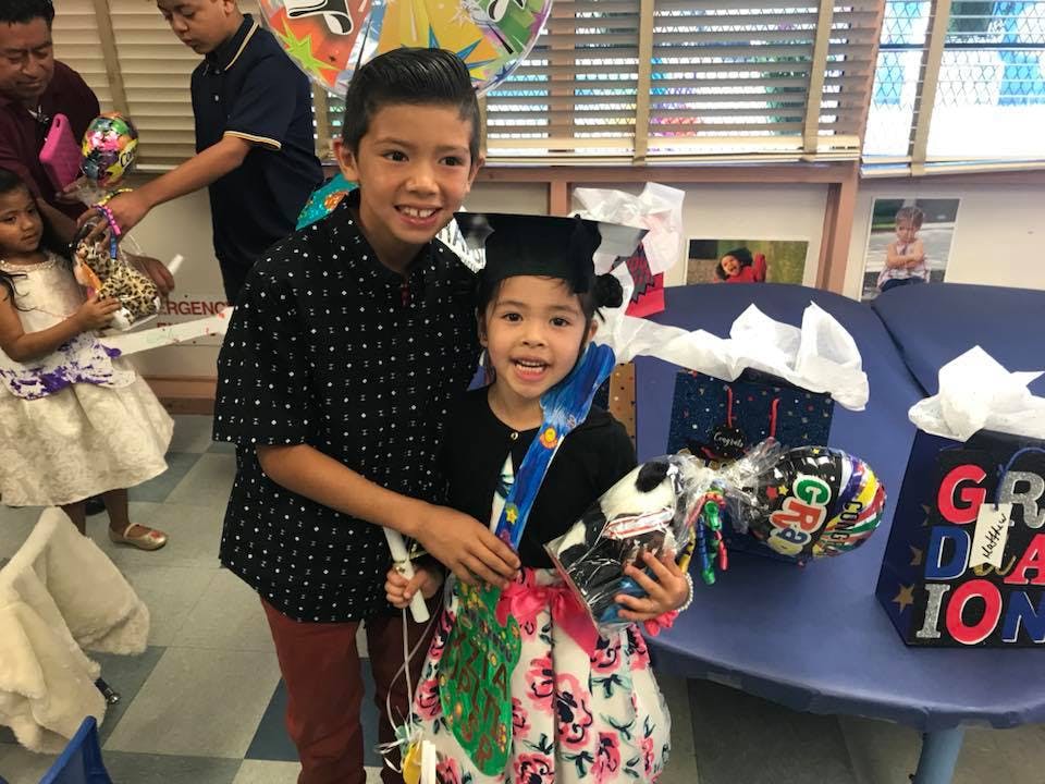 Two children, one wearing a graduation cap, holding gifts