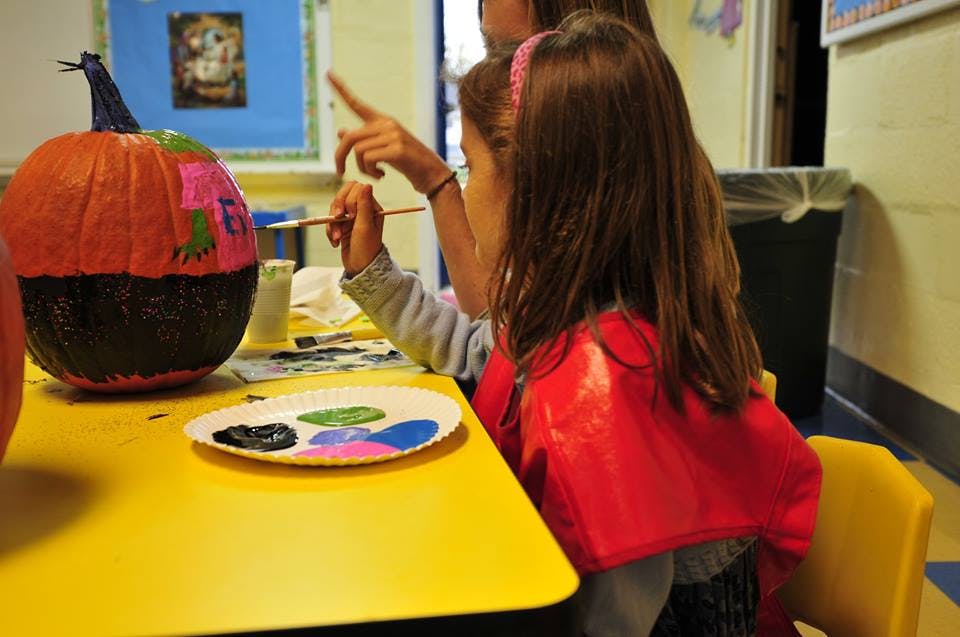 Child painting a pumpkin at a table