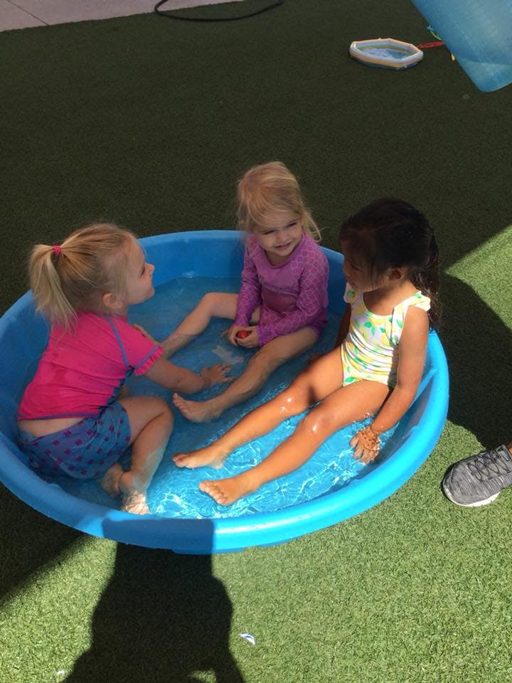 Three children sitting in a small blue wading pool