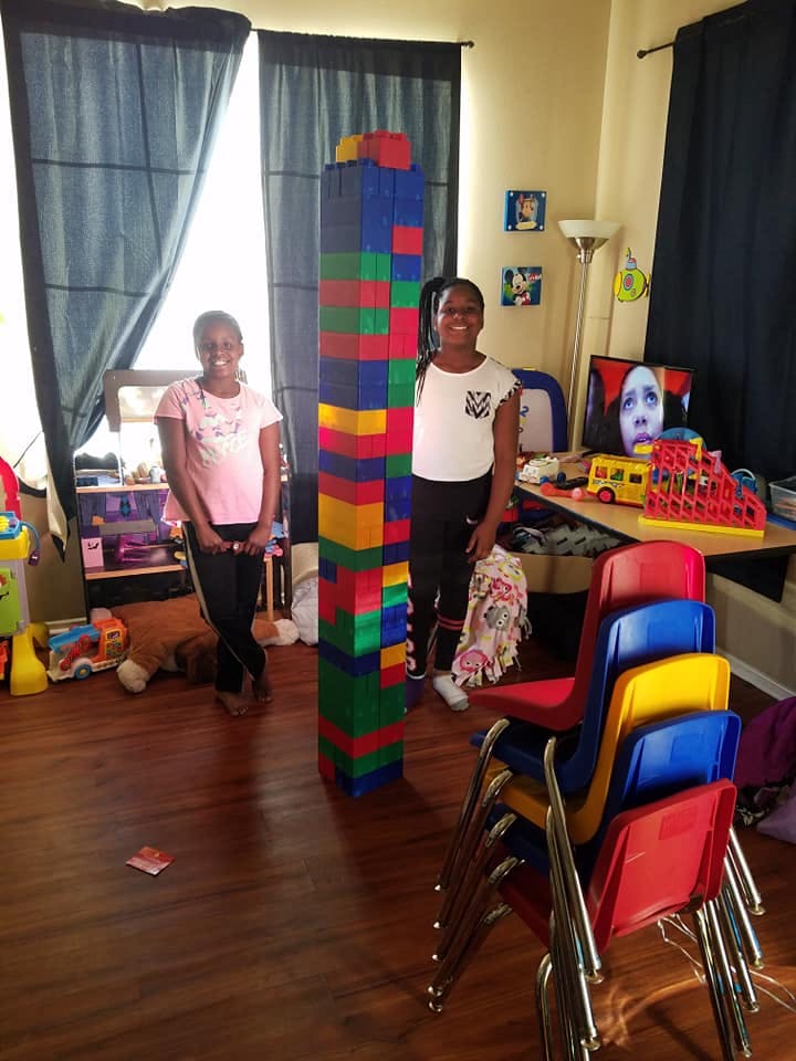 Two children standing next to a tall tower of colorful building blocks