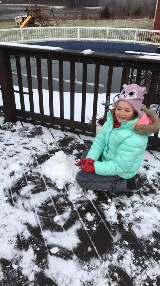 Child in winter clothing sitting on a snowy deck