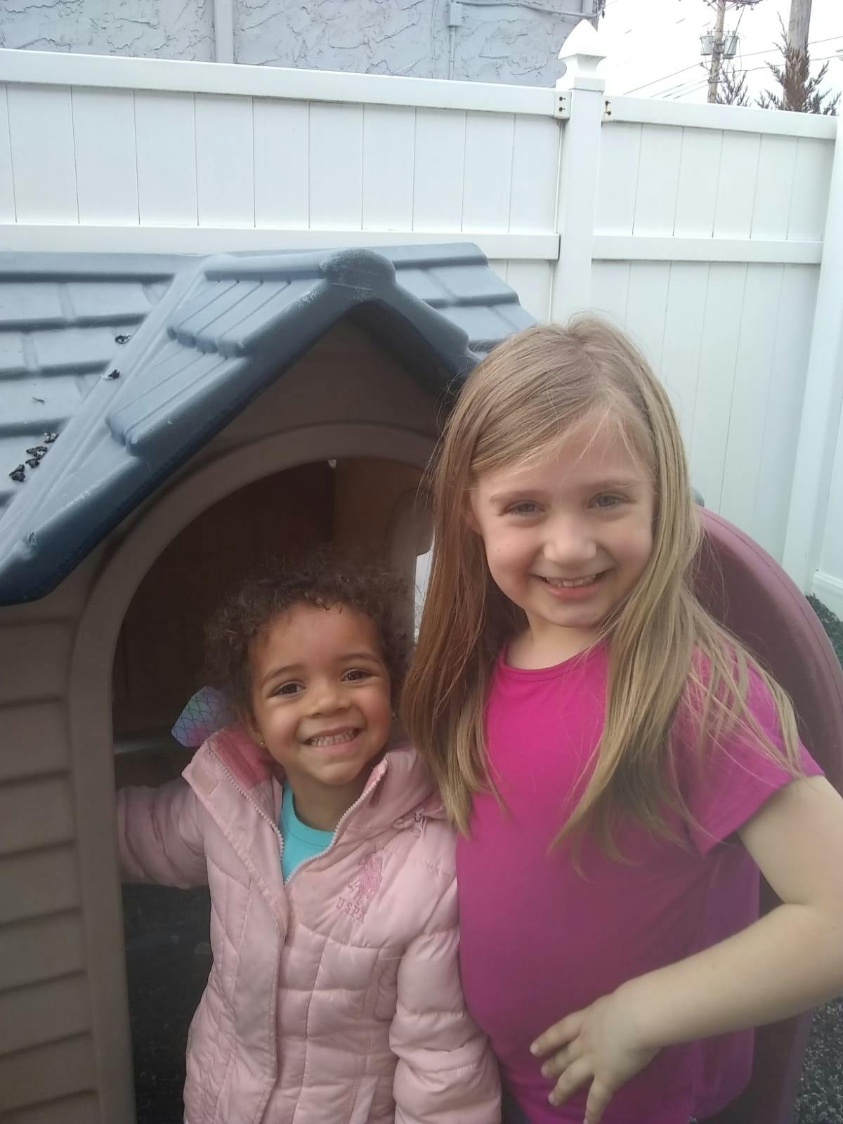 Two children smiling next to a playhouse