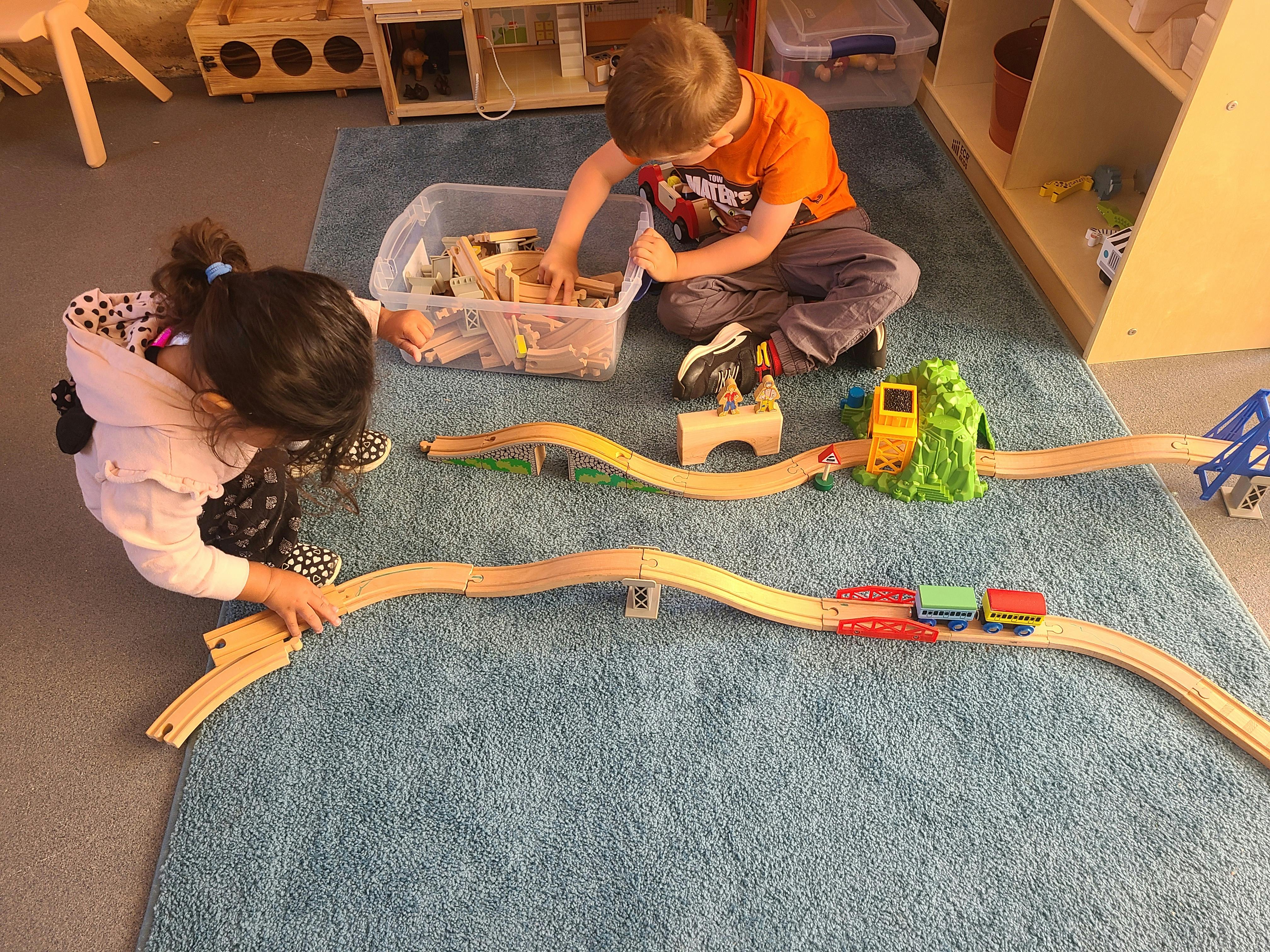 Two children playing with a wooden train set on a rug