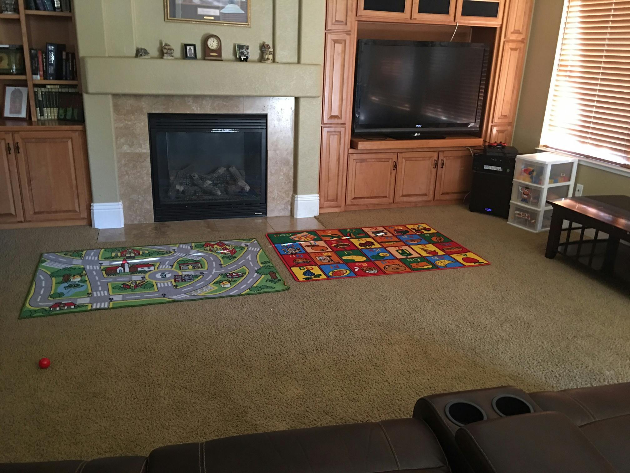 Two colorful playmats on a carpeted floor in front of a fireplace and TV