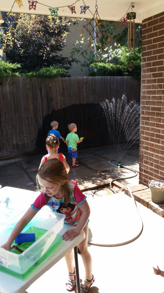 Child playing with water in a bin, other children near a sprinkler