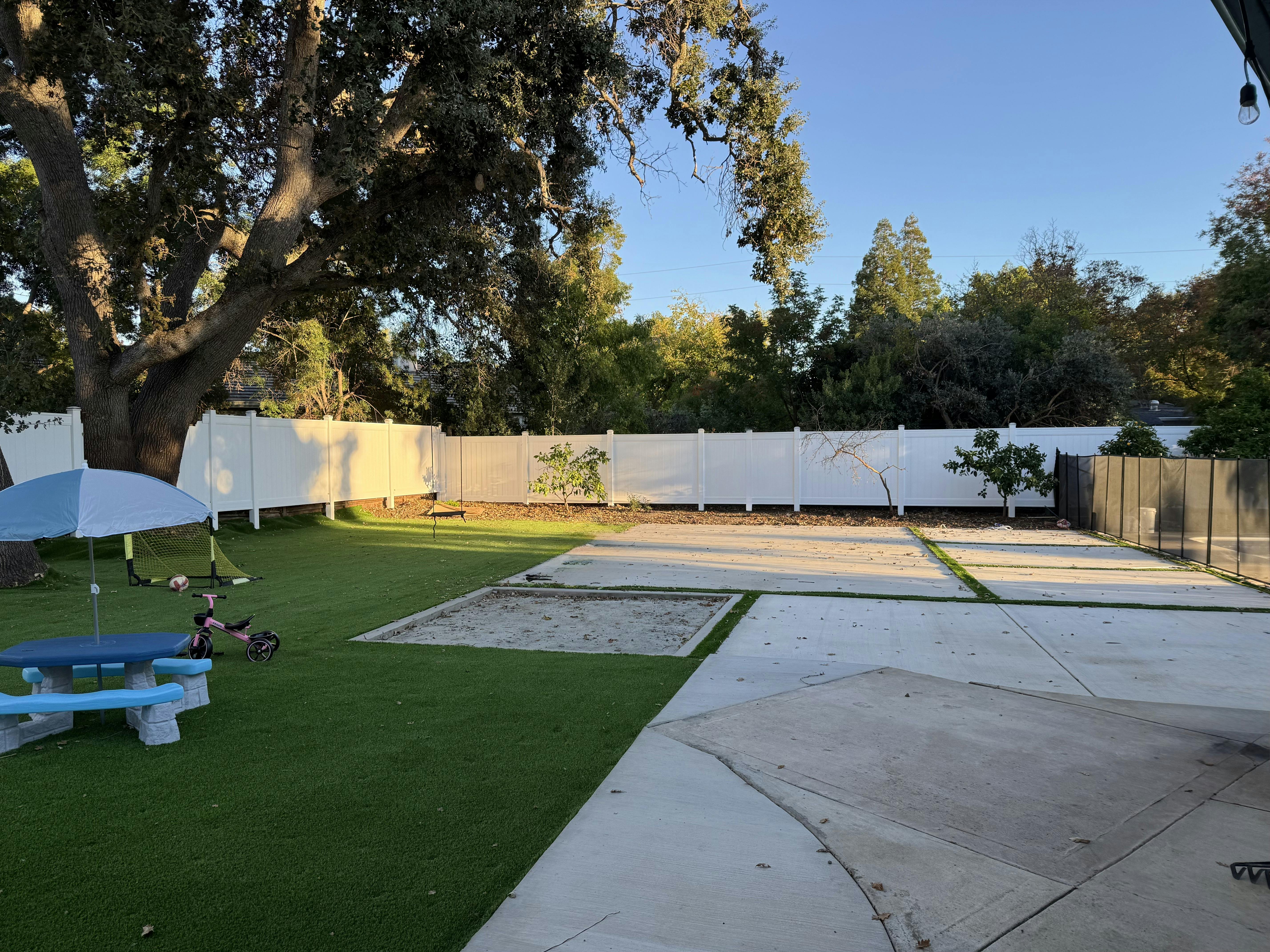 Backyard with artificial turf, concrete patio, sandbox, and picnic table